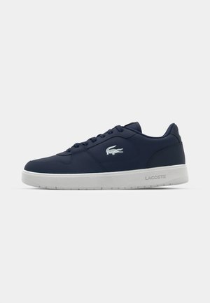 Marineblauwe leren sneakers met witte zool. Kenmerken zijn een ronde neus, vetersluiting en het Lacoste-logo aan de zijkant. Gladde textuur.