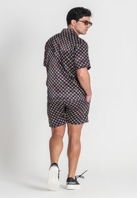 Schwarzes kurzärmliges Shirt und passende Shorts mit einem mehrfarbigen geometrischen Muster. Getragen mit weißen Sneakers, Ansicht von hinten.