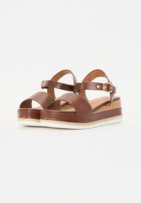 Brown leather platform sandals with an open toe, adjustable ankle strap, and woven jute detailing on the midsole. Flat, textured white outsole.