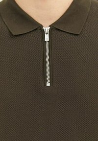 Hnedá polo tričko na zips vyrobené z textúrovaného materiálu, s plochým golierom a strieborným zipsom na krku.