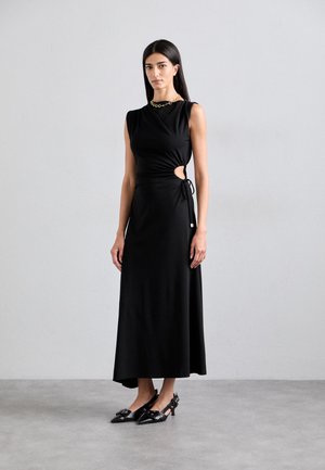Vestido negro ajustado con un detalle recortado en la cintura, tejido suave, diseño sin mangas y una silueta larga, combinado con tacones negros de punta.