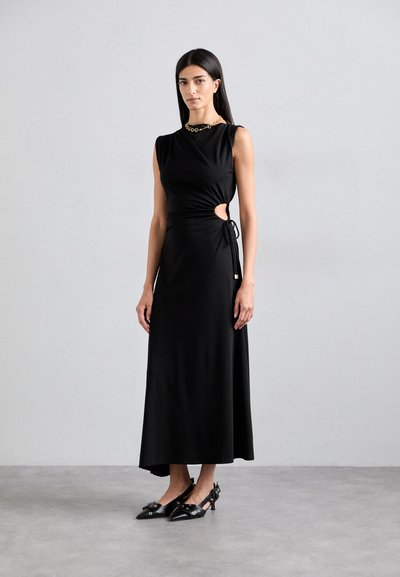 Black fitted dress with a cutout detail at the waist, soft fabric, sleeveless design, and a long silhouette, paired with black pointed heels.