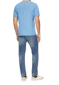 Jasnoniebieska koszulka z krótkim rękawem, wykonana z bawełny. Połączona ze średnio-washed dżinsami i białymi trampkami z brązowymi akcentami.