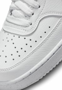 Białe sneakersy z podbiciem z teksturowanej skóry, perforowanymi detalami, płaskimi sznurówkami i gumową podeszwą z delikatnymi zadrapaniami.