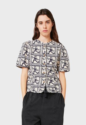Chemise à manches courtes avec une base crème présentant un motif géométrique noir. Boutonnage à l'avant et coupe décontractée, fabriquée en tissu coton léger.