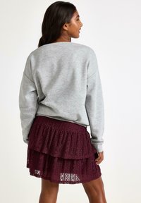Grå sweatshirt med dropped shoulders og en afslappet pasform, parret med en bordeaux lagdelt blondekjole med en flæsekant.