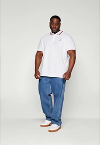 White polo shirt with red and blue accents, paired with loose blue jeans and white sneakers. Fabric appears smooth with a collar and logo detail.