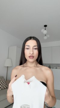 Hvit ribbet topp med en unik utskjæringsdesign, holdt av en person, som viser en jevn tekstur og en rød etikett inni.