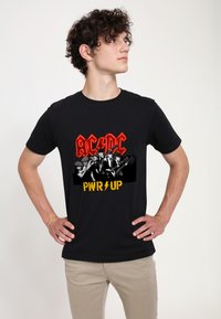 Černé bavlněné tričko s grafickým designem pěti hudebníků, s nápisem "AC/DC" v červené barvě a "PWR UP" v žluté barvě pod ním.