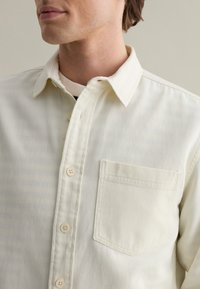Lichtbeige button-up shirt van gestructureerde stof, met een borstzak en een klassieke kraag, met zichtbare knoopdetails.