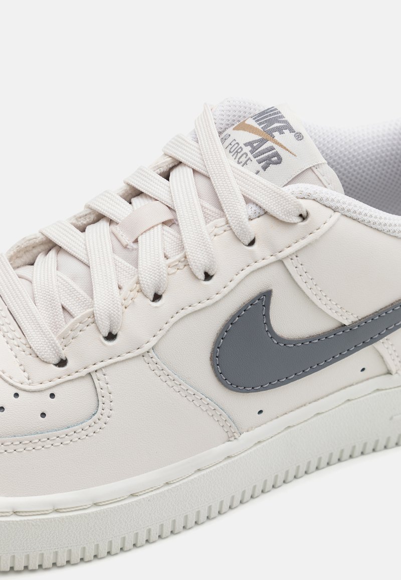 Sneakers Nike Air Force 1 con una tomaia in pelle beige chiaro, logo swoosh grigio, suola color crema e lacci testurizzati.
