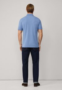 Gaiši zils polo krekls, kas izgatavots no kokvilnas, ar standarta apkakli un īsām piedurknēm, saskaņots ar tumši ziliem džinsiem un brūnām kurpēm.