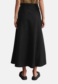 Jupe maxi en lin noir avec une texture lisse, des plis à l'arrière et une taille ajustée, associée à des chaussures noires à enfiler.