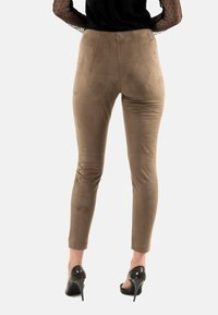 Leggings de ante marrón con un diseño ajustado, cintura de altura media y textura suave, combinados con tacones altos negros y una blusa de mangas transparentes con lunares.