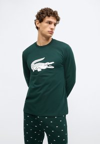Camiseta de algodón verde oscuro de manga larga con un gráfico blanco de cocodrilo en el frente, combinada con pantalones de pijama verdes oscuros con diseño estampado.