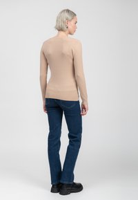 Beige Strickpullover mit langen Ärmeln, taillierter Passform und geripptem Saum, getragen mit dunkelblauen, geraden Jeans und schwarzen, klobigen Boots.