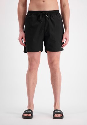 Zwarte zwembroek met een elastische tailleband en koord, voorzien van een soepele textuur en zijzakken, gecombineerd met zwarte instapsandalen.
