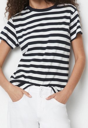 Czarna i biała T-shirt w paski z okrągłym dekoltem i krótkimi rękawami. Noszona z białymi spodniami, z lekko podwiniętymi rękawami i kieszenią.