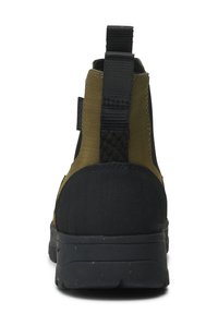Bota de tobillo resistente al agua que presenta una suela de goma negra, parte superior de tela en color verde oliva y una lengüeta para ponérsela fácilmente. Diseño de panel trasero texturizado.