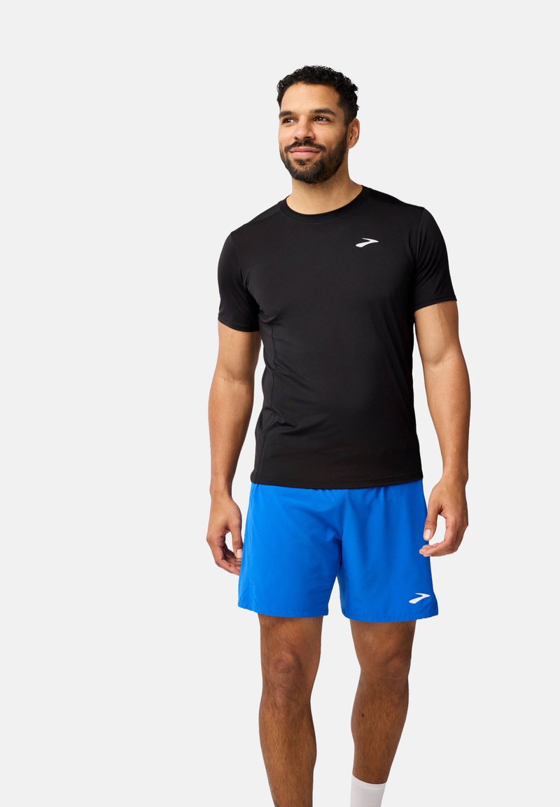 Mans aktivkläder-set bestående av en svart kortärmad tröja och blå shorts. Tröjan har en slim fit; shortsen är lätta med en vit LOGO.