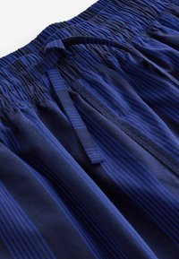 Marineblauwe shorts van zachte stof met verticale strepen in verschillende tinten blauw, een elastische tailleband en een trekkoord.