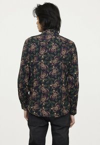 Langsleeve shirt met een donker bloempatroon in groen, paars en beige, gemaakt van een lichte stof met een kraagontwerp.