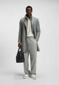 Harmaa kuviollinen takki, jossa on lovi-aines, kermaontelokudottu villapaita, harmaat housut ja musta nahkalaukku. Urheilulliset valkoiset lenkkarit.