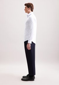 Biała koszula z cienkimi niebieskimi paskami, długimi rękawami, z wykładanym kołnierzykiem, w połączeniu z ciemnymi, dopasowanymi spodniami i czarnymi butami.