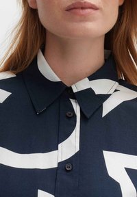 Chemise bleu marine avec un motif abstrait blanc, dotée d'un col, d'une fermeture boutonnée et de détails de couture visibles. Texture lisse.