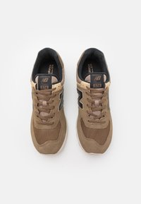 Baskets New Balance 574 marron avec une tige en suède texturé et mesh, bout rond, accents noirs et lacets beige. Design classique, col rembourré.