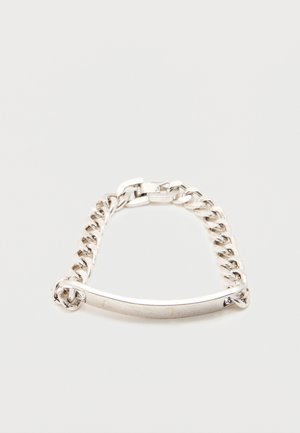 Ezüst lánc karkötő középen egy üres, ívelt fém tábla, fehér háttéren.