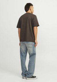 Camiseta de algodón marrón oscuro de manga corta, combinada con jeans de corte suelto azul claro. Zapatillas negras con suelas blancas completan el atuendo.