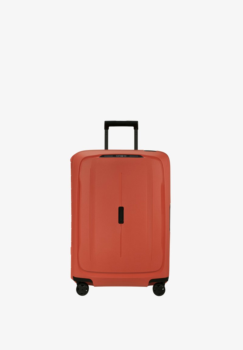 Grande valise rigide en corail avec une poignée rétractable noire et quatre roues pivotantes, se tenant droite sur un fond blanc.