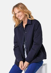 Marineblaues gepolstertes Jacke mit Knopfverschluss, spitzem Kragen und Seitentaschen. Glatte Textur, lange Ärmel mit einem dezenten Logo auf dem Arm.