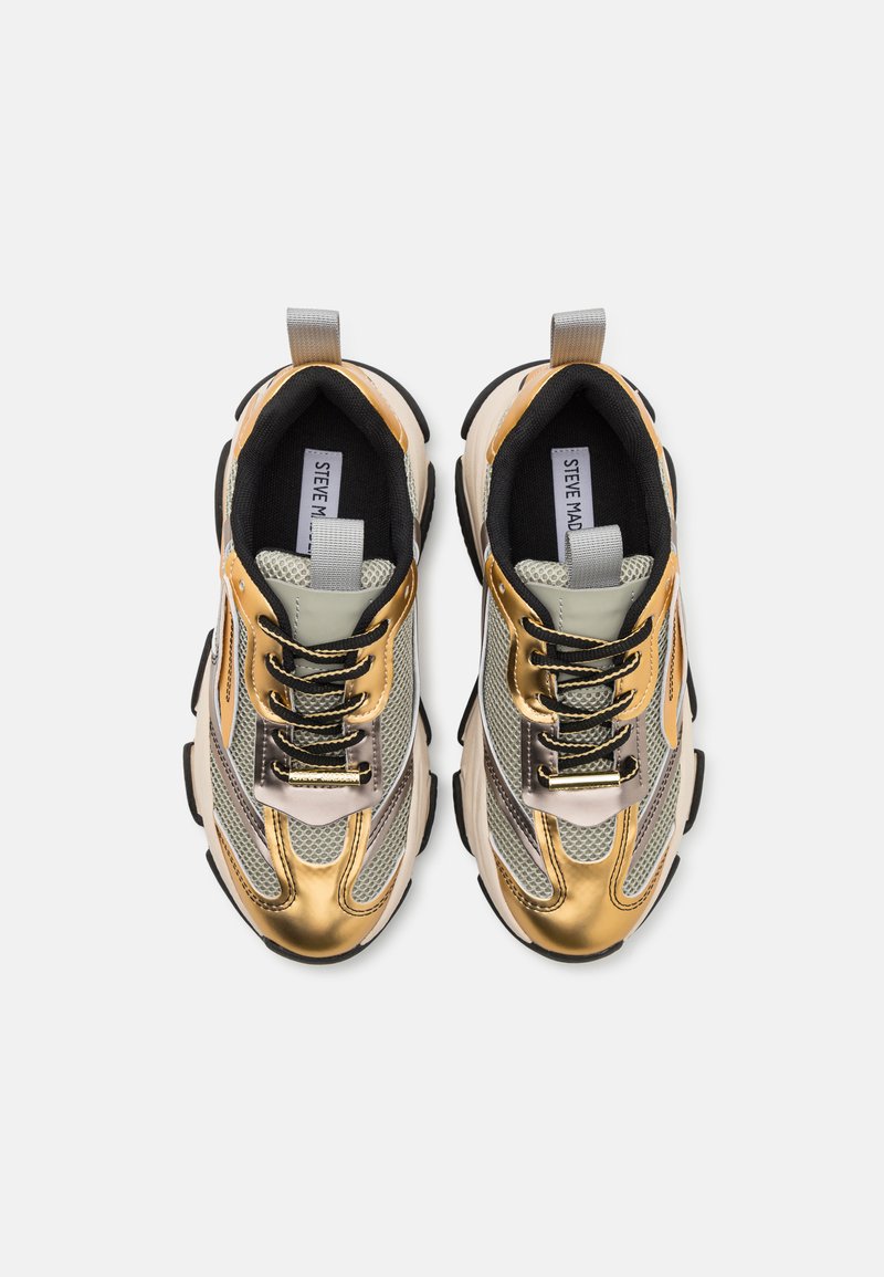 Zapatillas con cordones con un diseño metálico en oro y plata, paneles de malla, detalles en negro y una suela negra gruesa. Cuenta con una lengüeta para ponerlas y quitarlas fácilmente.