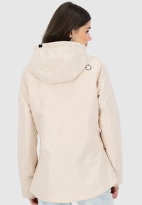 Giacca beige chiaro con cappuccio, alla moda, con texture liscia e dettaglio del logo sulla spalla. Presenta una vestibilità comoda e maniche lunghe.