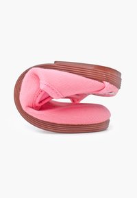 Calzado de tela rosa tipo slip-on con suela de goma marrón contorneada, que presenta una parte superior texturizada y una forma redondeada.