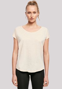Light beige crew-neck t-shirt with short sleeves, soft texture, and a relaxed fit, paired with black leggings. Smooth fabric with no patterns.