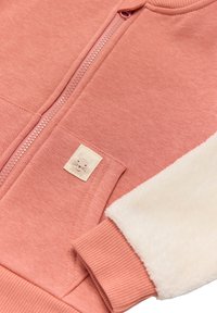 Sudadera rosa con cremallera en la parte delantera, mangas de felpa crema suave, puños acanalados y un pequeño parche de tela con un diseño de conejo.