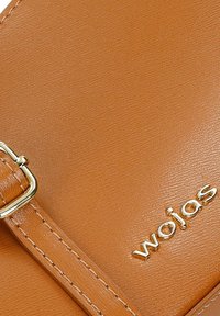 Sac bandoulière en cuir tan avec une boucle en métal doré et un logo en relief. Texture lisse avec des détails de couture visibles.
