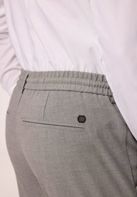 Harmaat joustavat vyötäröhousut, joissa on sileä pinta, takatasku ja pieni musta logoyksityiskohta vyötärön ympärillä.