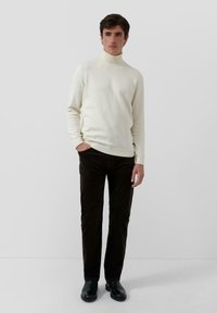Cream turtleneck sweater made of knit fabric, paired with dark brown corduroy pants. The outfit features a fitted silhouette and minimal detailing.