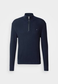 Pull en maille bleu marine à manches longues avec une fermeture éclair au quart et un petit logo rouge, blanc et bleu sur la poitrine gauche.