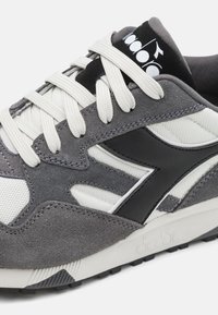 Gray athletic shoe featuring a combination of suede and mesh material, white laces, black leather accents, and a padded tongue with logo.
