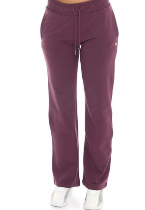 Modèle portant un pantalon de jogging ample couleur prune, avec une taille à cordon de serrage et des baskets blanches, sur fond blanc.