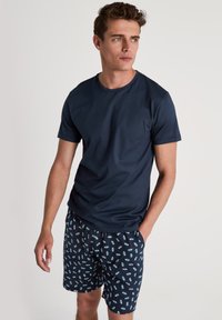 Navyblauwe T-shirt met korte mouwen van gladde stof, gecombineerd met gestreepte shorts met ijsje motieven op een donkere achtergrond.