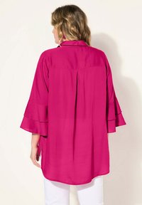 Fuchsia Langarmbluse mit Rüschensäumen, geradem Schnitt und seitlichen Schlitzen. Hergestellt aus leichtem Stoff mit glatter Textur.