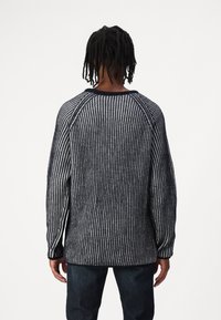 Der übergroße Pullover in Marineblau und Weiß mit gestreiftem Muster weist eine gerippte Textur, Raglanärmel und einen abgerundeten Ausschnitt auf. Die Rückansicht zeigt die Länge und die lockere Passform.