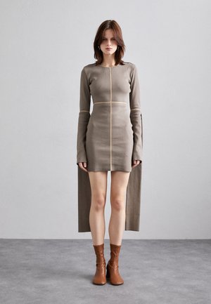 Robe en tricot taupe avec des manches longues et une fente sur le côté, dotée de coutures contrastées beige. Associée à des bottes chelsea marron.