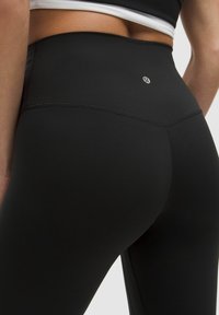 Leggings negros de cintura alta confeccionados en una tela elástica, con una textura suave y un sutil detalle del logo por encima de la cinturilla.